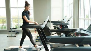 Woman walking on a treadmill during workout in the gym with headphones around her neck
