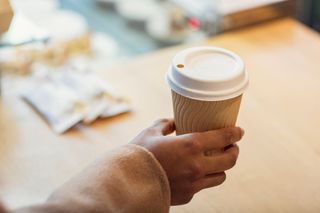 Hand holding fibre packaging coffee cup by Huhtamaki, blurred surroundings in the background
