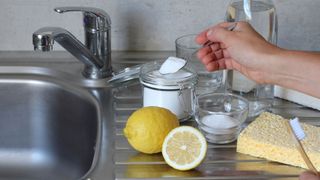 A stainless steel sink with baking soda, lemons and vinegar on the side, ready to clean