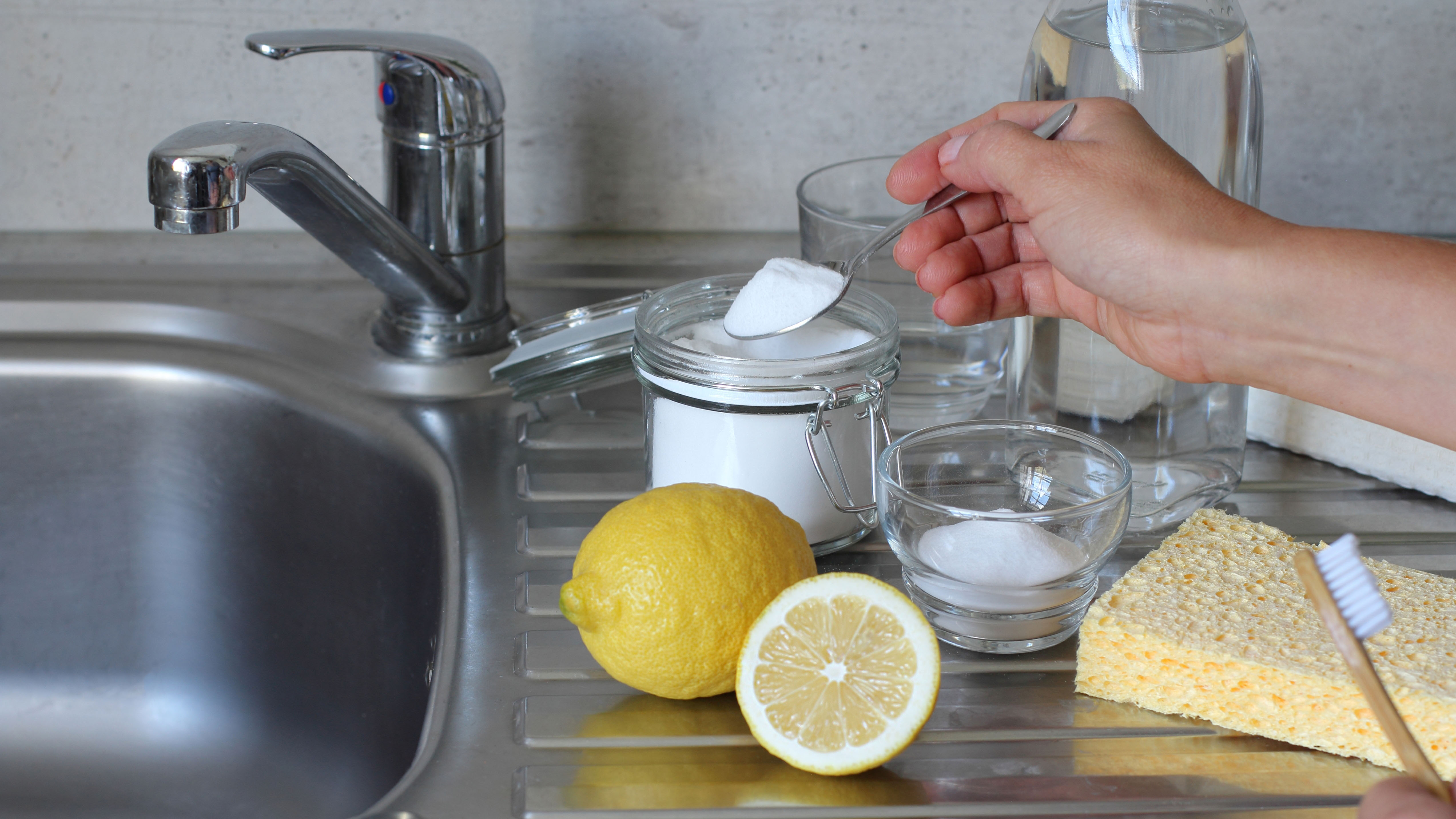 A stainless steel sink with baking soda, lemons and vinegar on the side ready for cleaning