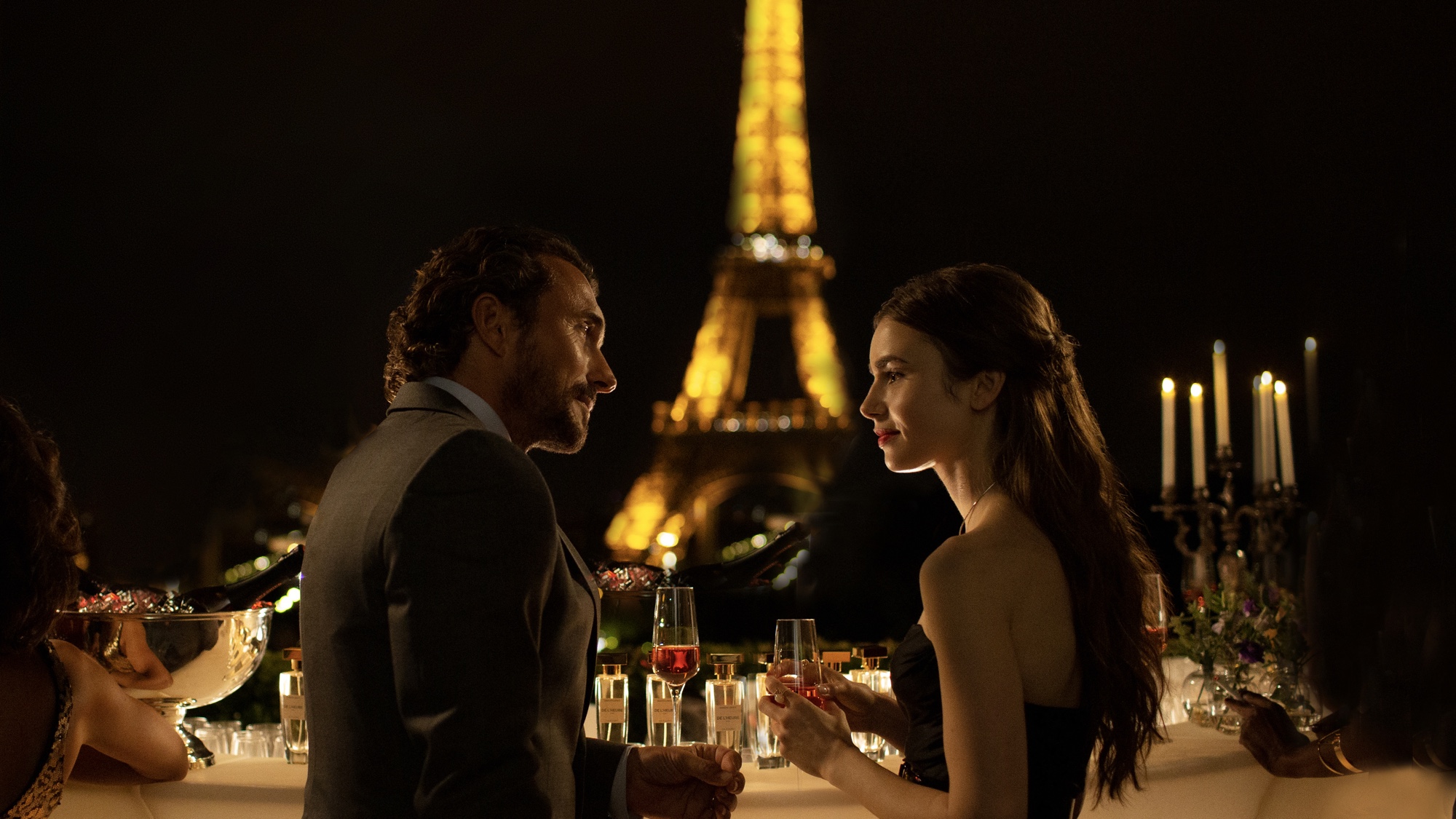 William Abadie (L, as Antoine) and Lily Collins (R, as Emily Cooper) gazing into each other's eyes in front of the eiffel tower in emily in paris