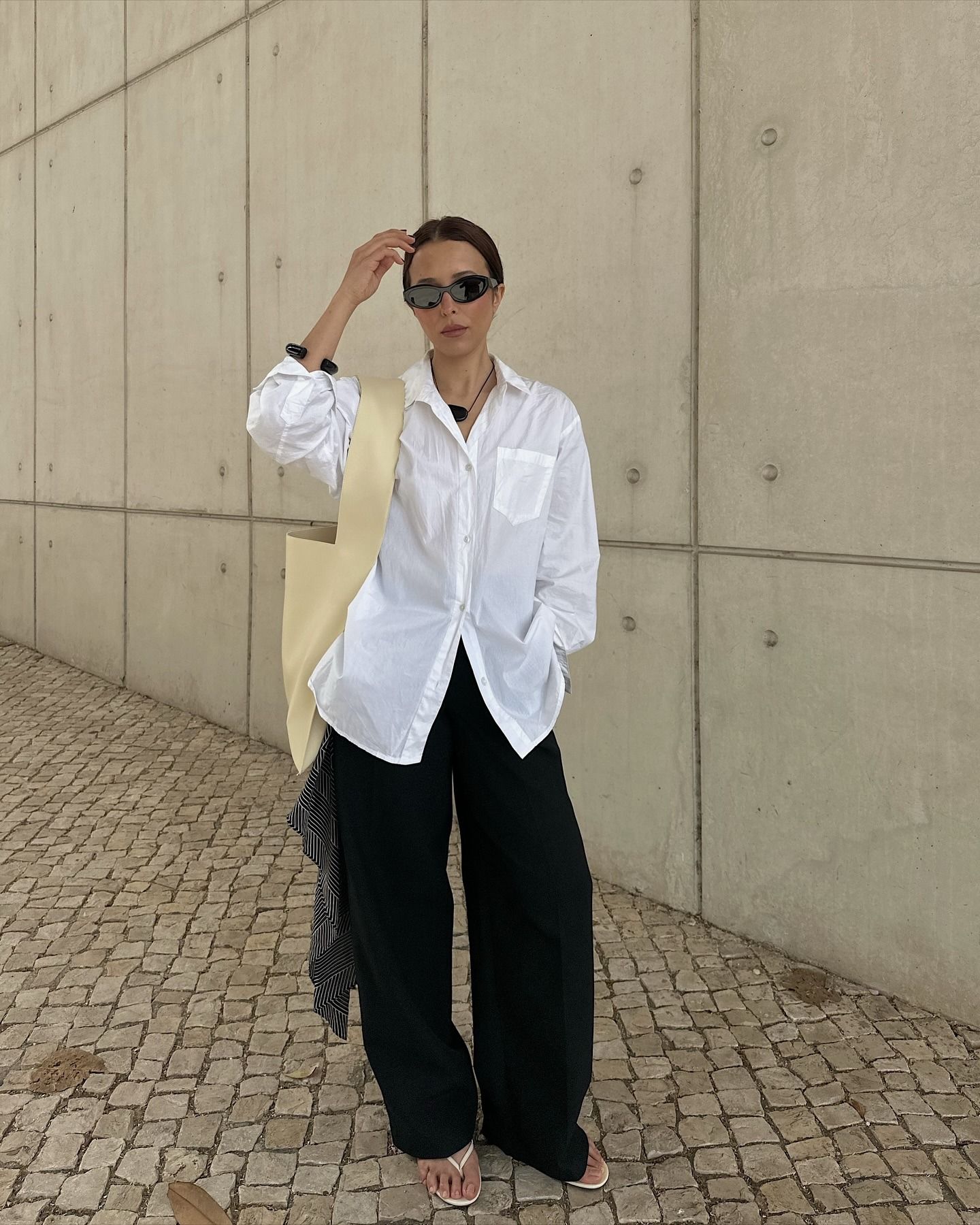 Debora wears a white button-down shirt, black pants, and white flip-flops.