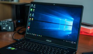 An Asus laptop displaying the Windows 10 splash screen sitting on a desk.