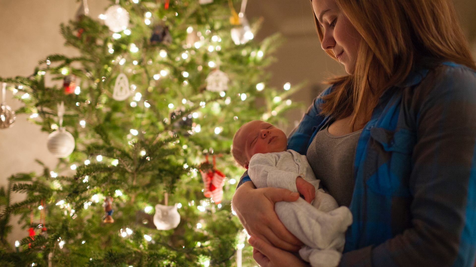 A mother holds a baby by a Christmas tree