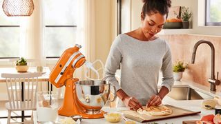 KitchenAid stand mixer on a kitchen countertop with a woman preparing a pizza