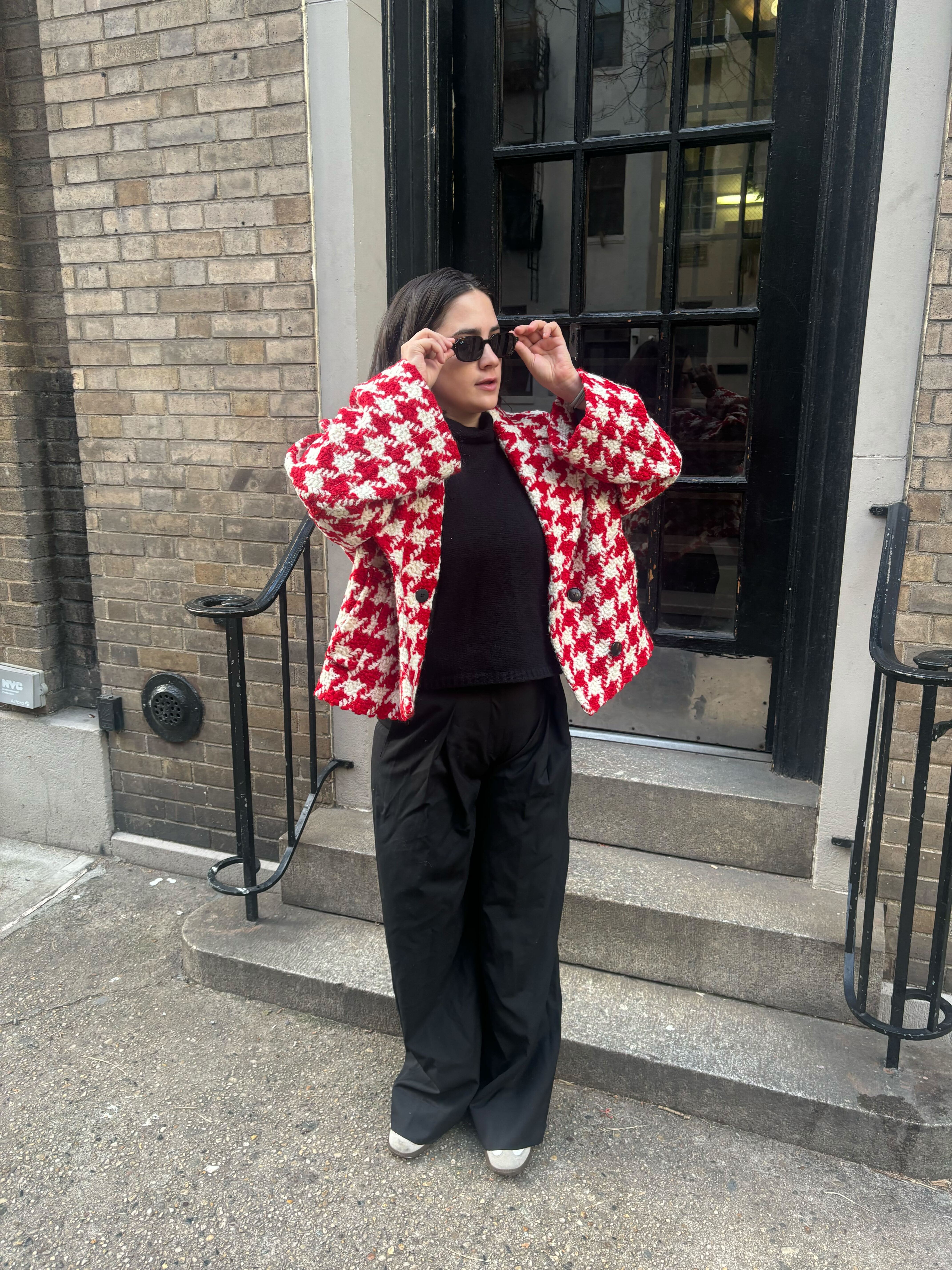 Julia Marzovilla wearing sunglasses and standing in front of a door, with a red checked jacket and black pants
