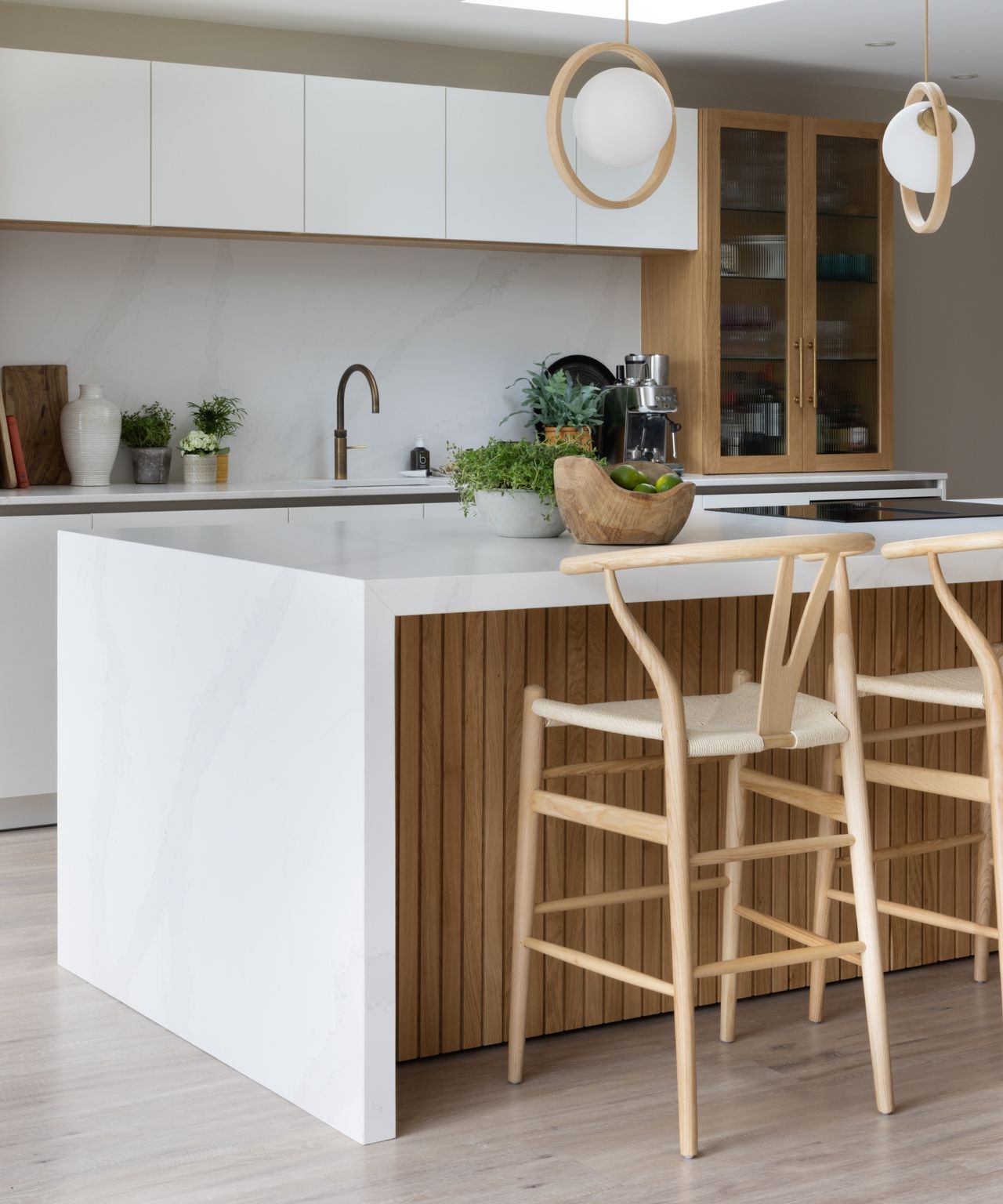 Kitchen island with white marble waterfall end, slatted oak panelling, wishbone stools and wood-ringed globe pendants