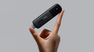 A hand holding a Xiaomi TV Stick 4K (2nd gen) in front of a grey background