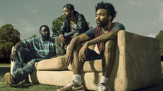 A still from the TV show Atlanta in which the main characters are sat outside on a settee.