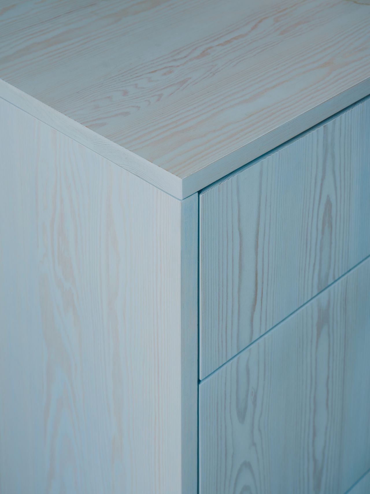 Close-up image of the corner of a cabinet. The cabinet is a natural wood stained with a light blue wood stain.