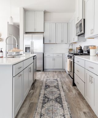 A white kitchen with shelving and cabinets and a wooden floor with a runner rug