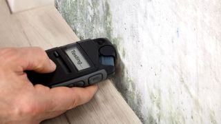 Mould testing device held in hand against a mouldy wall