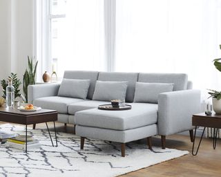 Gray modular sofa in modern living room, cream rug, dark wood floor, plants and side tables