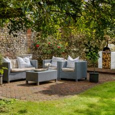 Garden sofas arranged on brick floor tiles in the corner of a garden by a garden wall