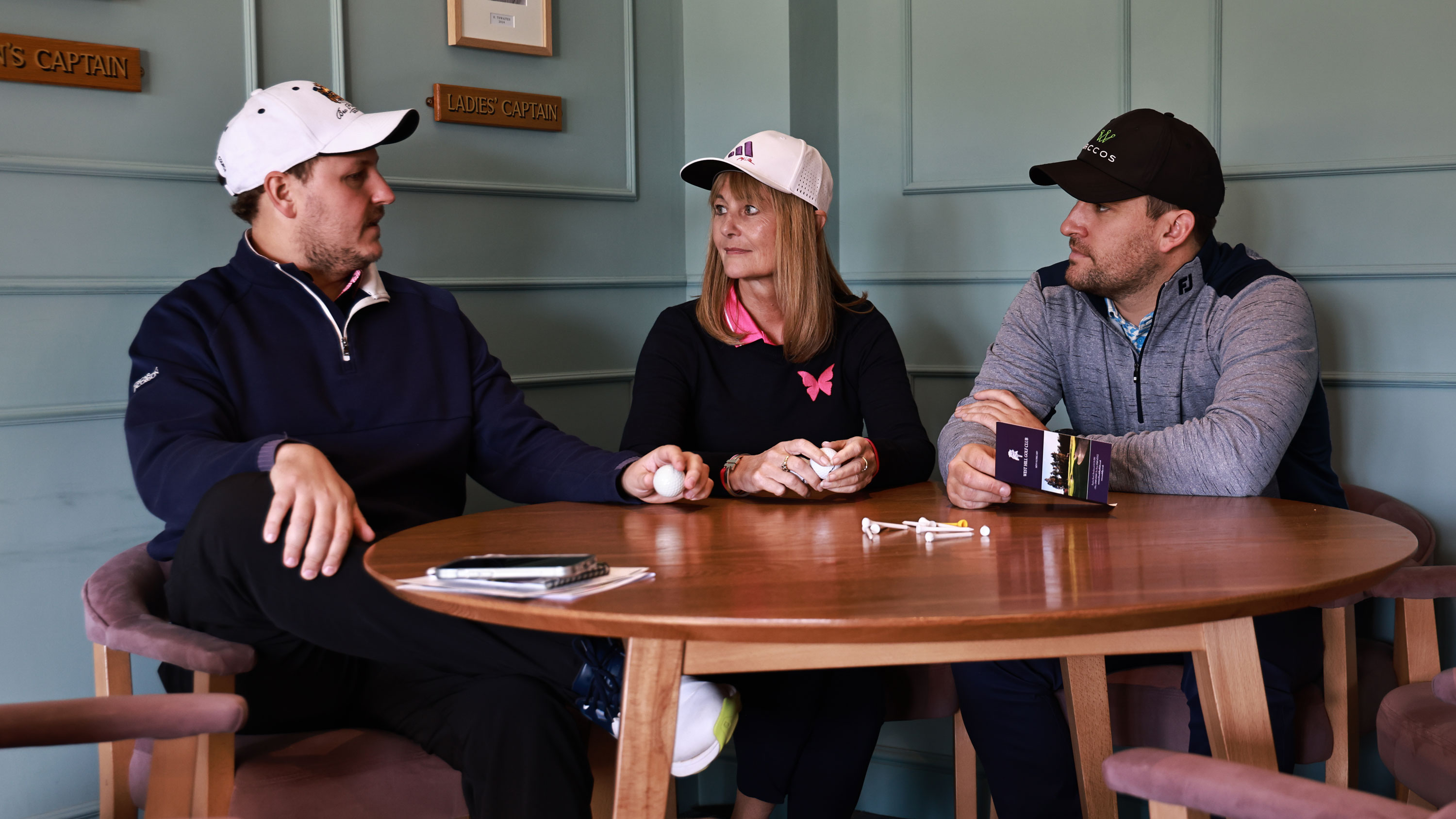 three golfers inside the clubhouse wearing hats