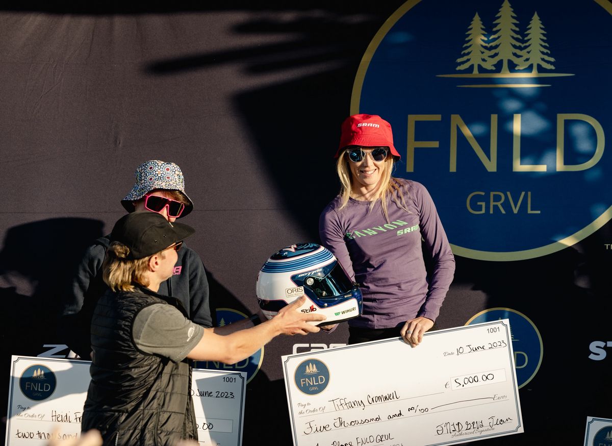 F1 driver and co-race founder Valtteri Bottas (left) presents the winner's helmet to Tiffany Cromwell at 2023 FNDL GRVL
