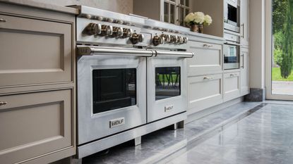 A double silver oven and stove set up on a kitchen with marbel floors and blush pink cabinets 