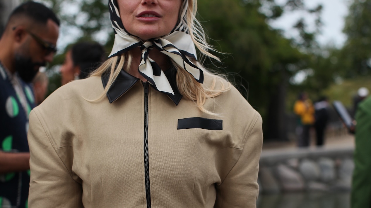 A Guest is seen wearing a beige barn jacket with a silk head scarf at the MKDT Studio show. 