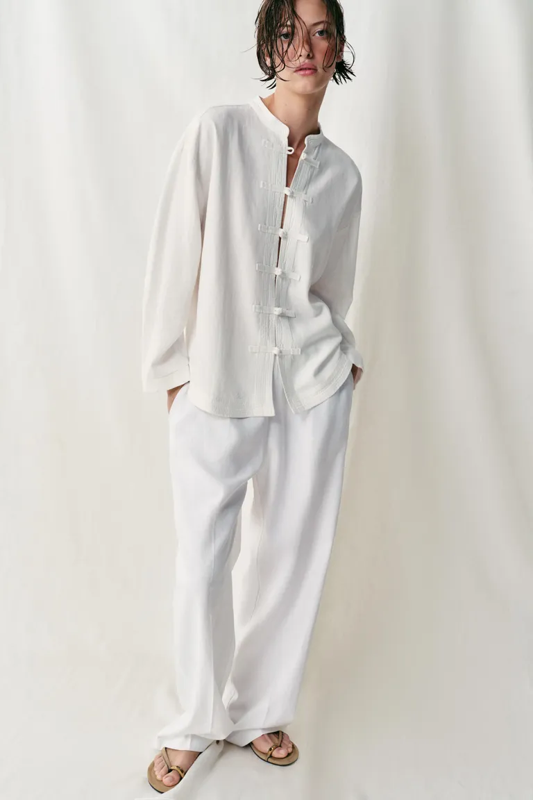 Woman wears white top, white trousers and beige sandals