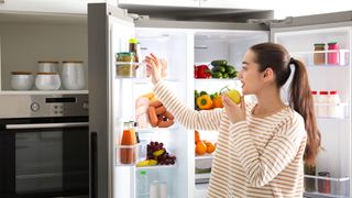 Woman eating apple with refrigerator doors open