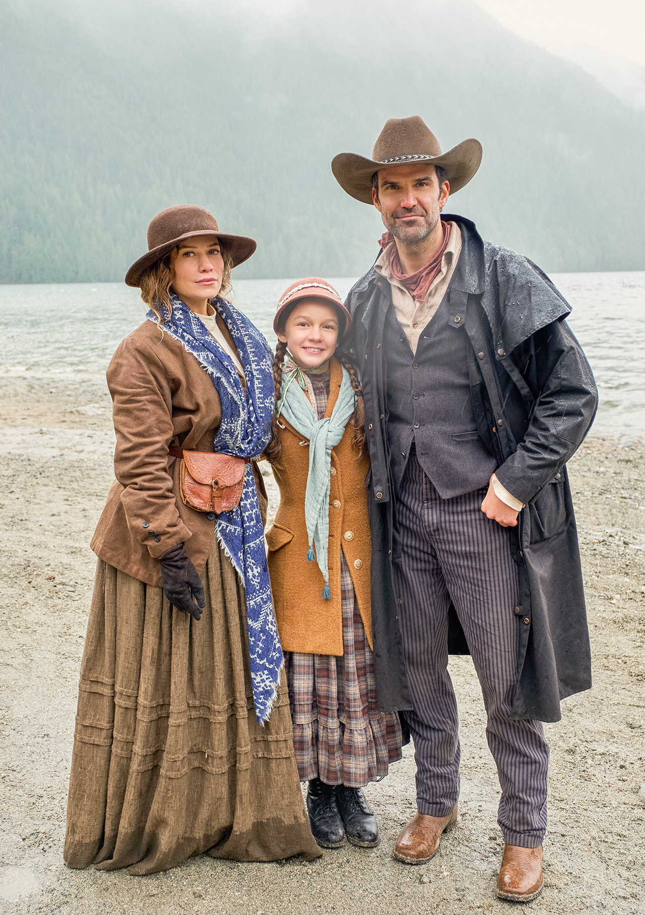 ビーチの砂の上に立つベサニー・ジョイ・レンツ、ベンジャミン・エアーズ、ミラ・モーガンのプレス写真。レンツのスカートは泥だらけで濡れています。彼らは皆、フロンティアの装備と帽子をかぶっています。