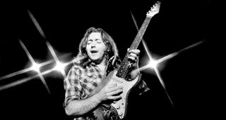 A black and white photo of Rory Gallagher onstage with his battered Fender Strat