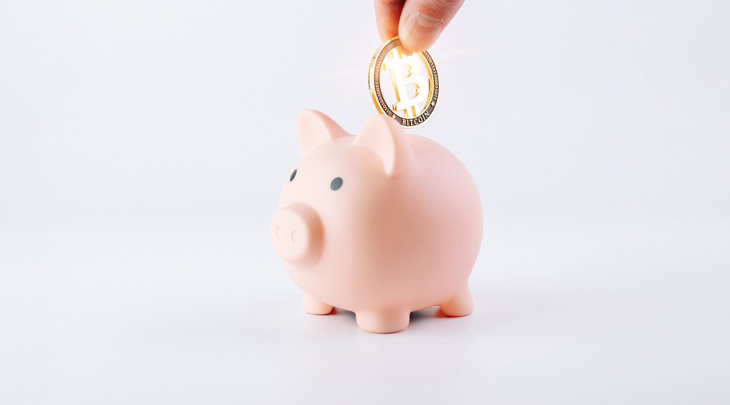 Hand depositing a Bitcoin cryptocurrency coin into a piggy bank representing pensions, retirement planning and savings