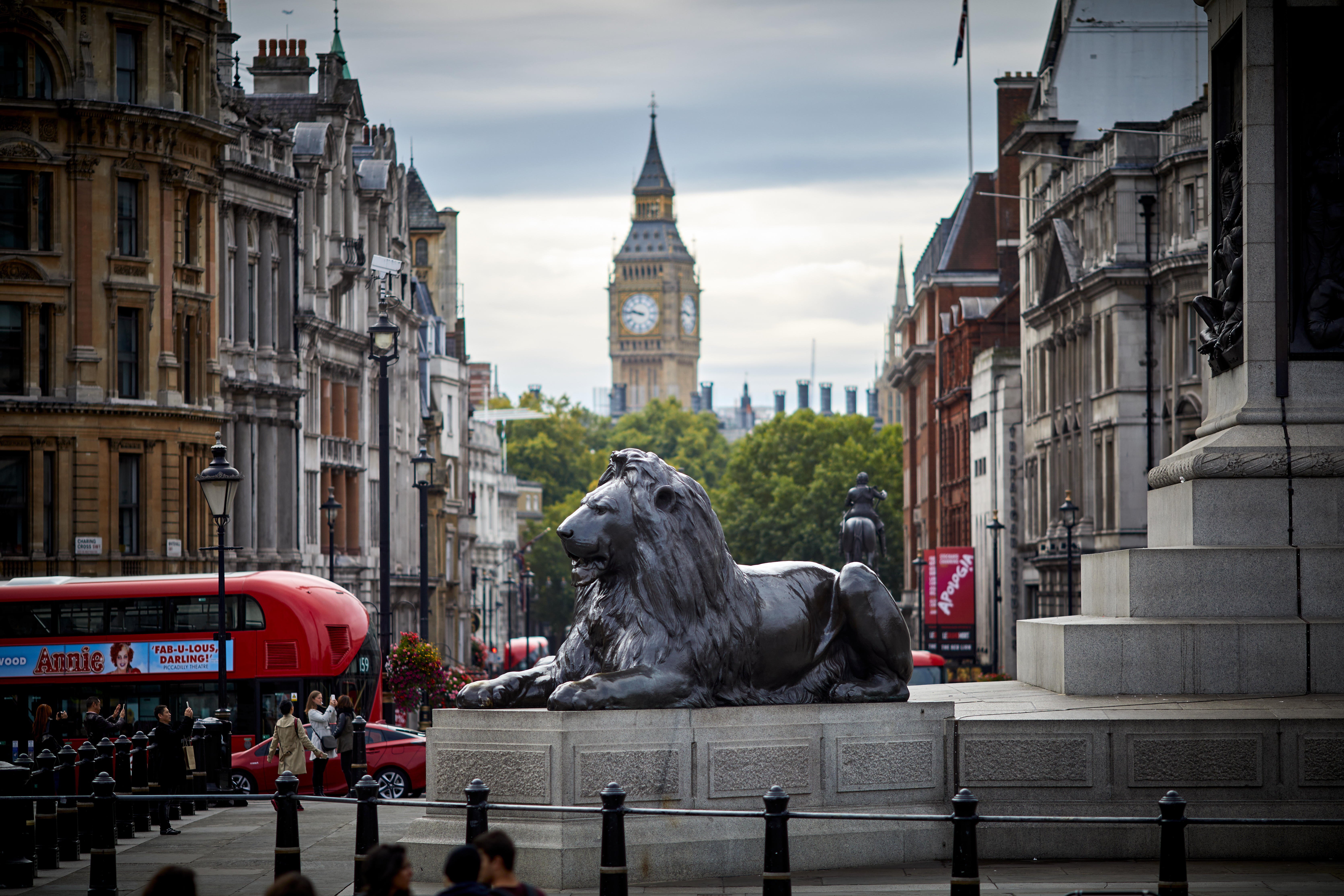 A lion at the foot of Nelson's Column with a red London bus and Big Ben in the background