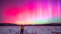 Photo of a person stood in front of pink auroras in China