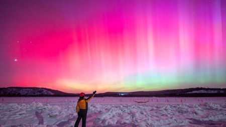 Photo of a person stood in front of pink auroras in China