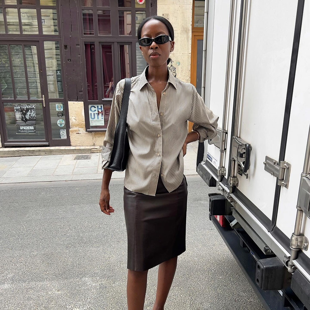 a woman wearing a striped shirt, brown leather skirt and bag