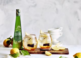 A Bottlegreen bottle next to two drinks with apple slices in