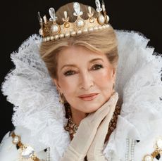 Martha Stewart wearing a ruffled white head dress and crown leaning her head in her hands