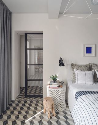 A bedroom with a black framed glass door and a white, gray and black geometric tiled floor