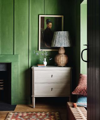Rattan table light with fabric lampshade on chest of drawers and green walls