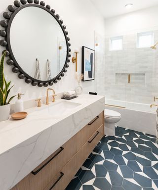 Round wooden detail mirror in narrow white bathroom with geometric black and white tile floor