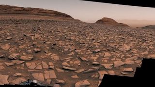 a partial panoramic view of a rusty landscape with large broken rocks embedded in the redbrown ground.