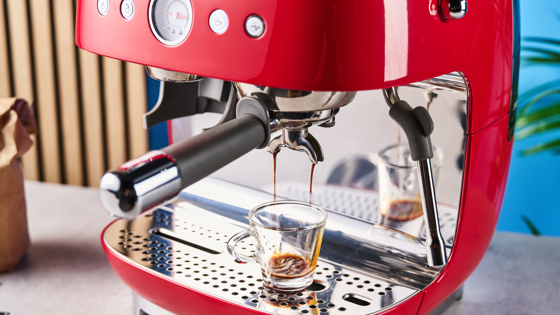 a red smeg espresso machine with burr grinder is photographed against a blue background
