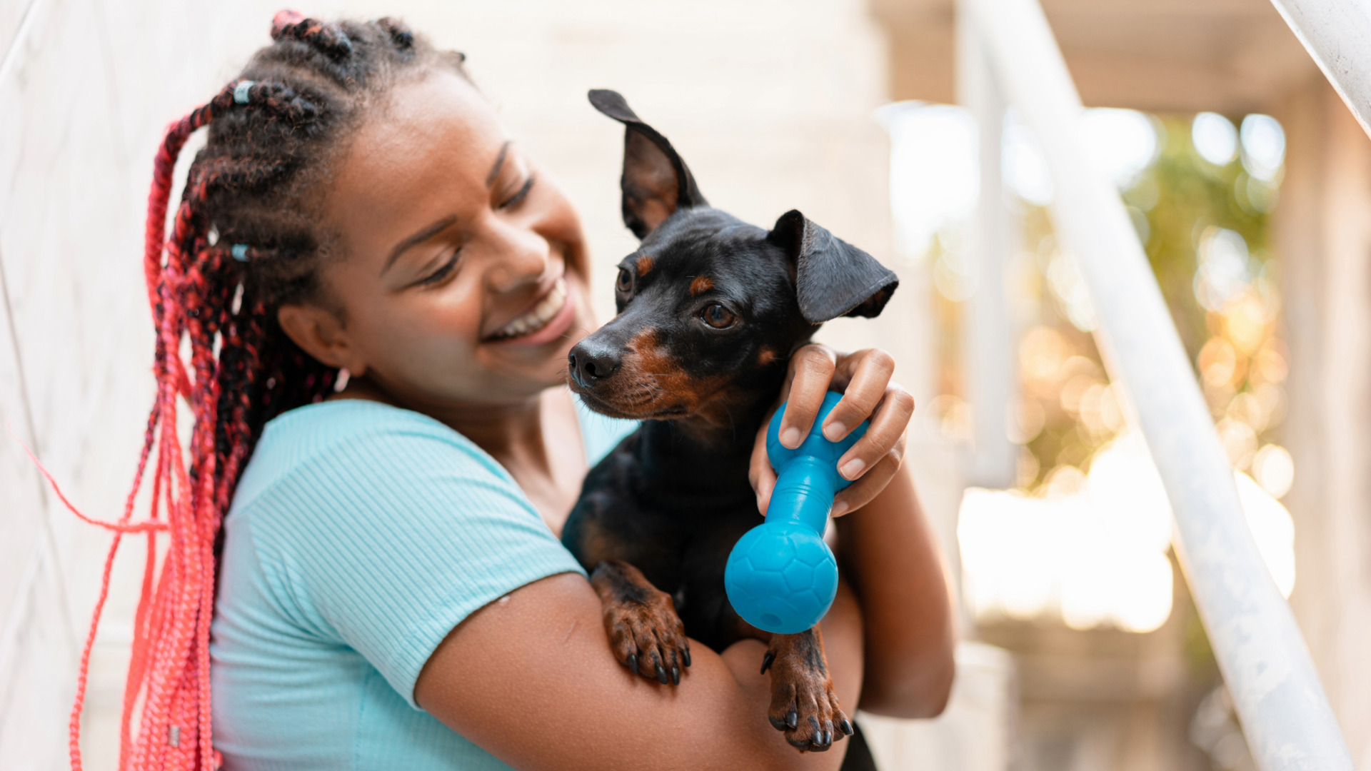 smiling woman holds a small black and brown dog and a blue dog toy