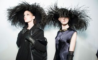 Two models wearing dark clothes featuring feathers and a headpiece