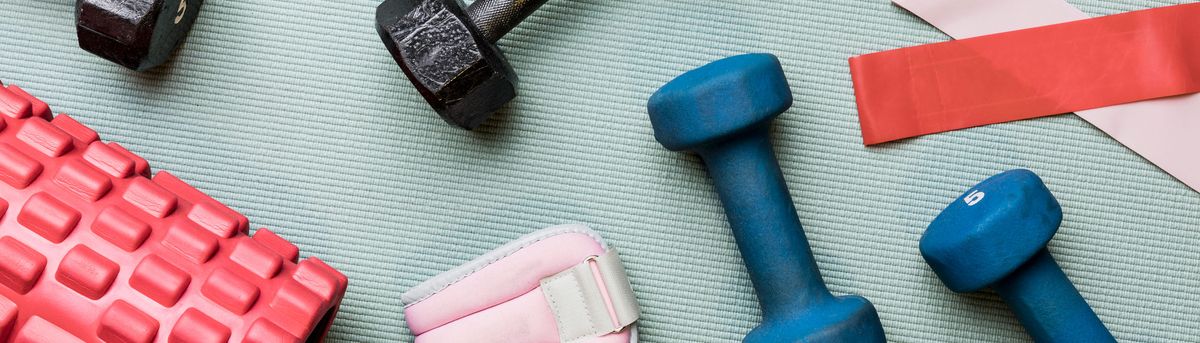A close-up picture of dumbbells, resistance bands and a foam roller laying on a yoga mat