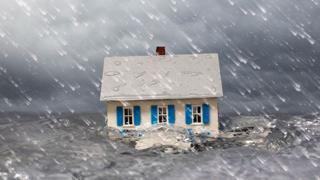 White single family house partially submerged in turbulent water with a stormy sky and wind blown rain