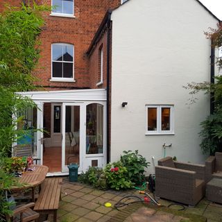 house exterior with red brick and white wall white door plants wooden bench