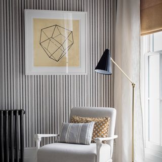 A corner of a living room with a wall covered in a vertically striped wallpaper with a framed art work hung on it