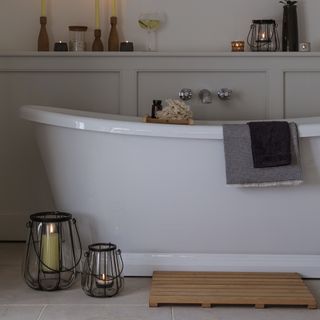 White bath with wooden bath mat and panelling on walls