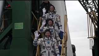 Three astronauts wave farewell as they prepare to board their Russian rocket.
