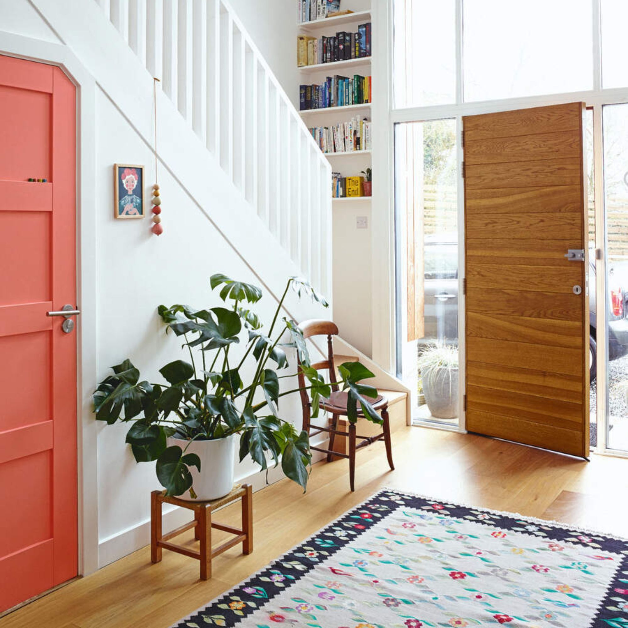 White painted hallway with a pink door to an under cupboard stairs and a colourful rug on the floor