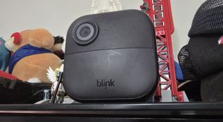 A Blink Outdoor 4 wireless security camera sitting on a shelf