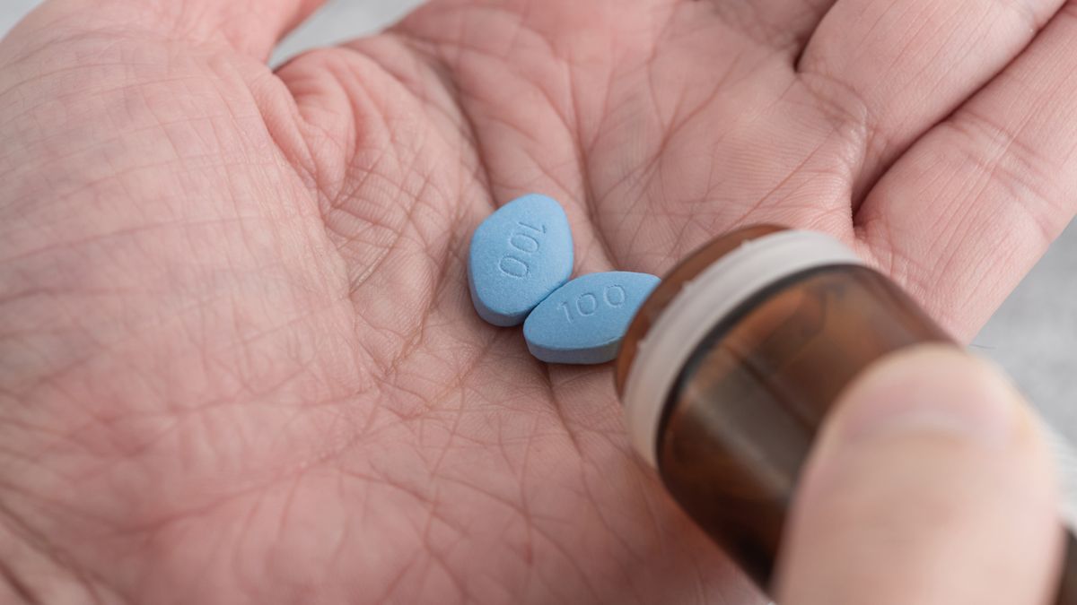 Close up of a man&#039;s open palm as he pours out two Viagra pills from a pill bottle