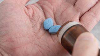 Close up of a man's open palm as he pours out two Viagra pills from a pill bottle